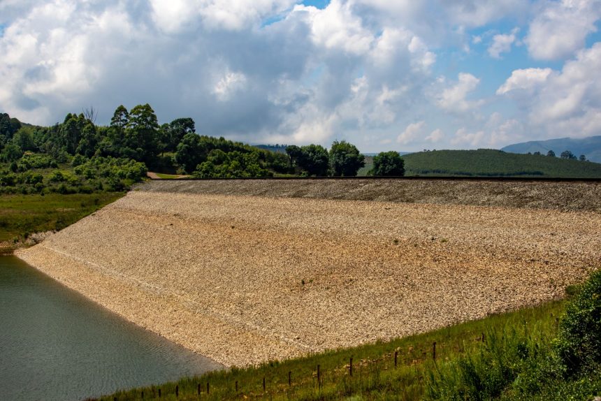 Barragem em paisagem rural, cercada por vegetação sob céu claro.