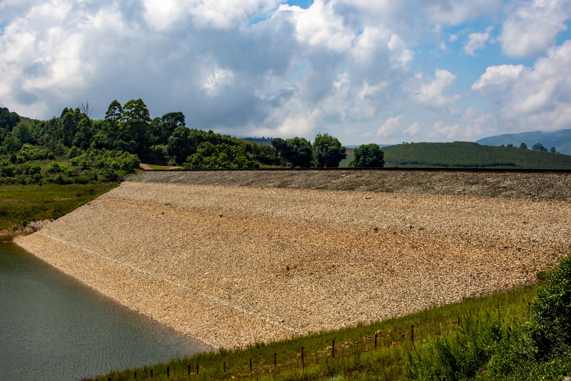 Barragem em paisagem rural, cercada por vegetação sob céu claro.