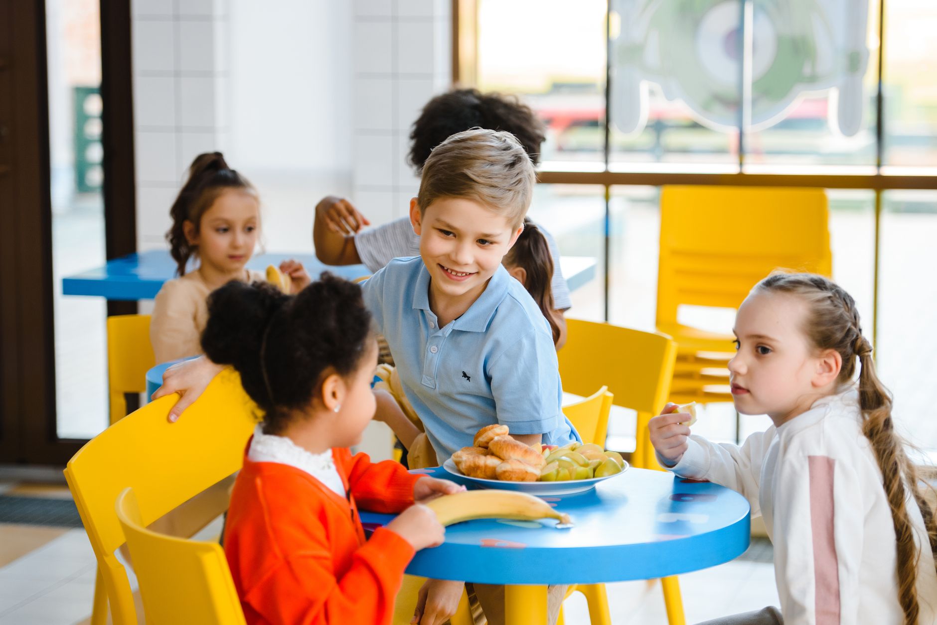 Grupo de crianças almoça junto em uma cafeteria escolar iluminada.