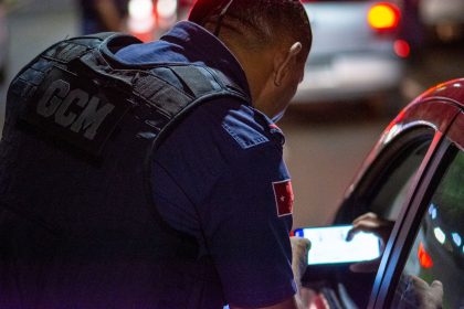 Agente de segurança confere documentos de um motorista durante fiscalização de trânsito à noite.