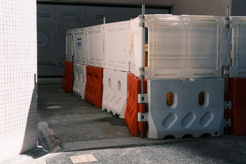 Barreiras plásticas vermelhas e brancas bloqueiam parcialmente uma via urbana.